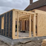Extension de maison en bois : ce qu'il faut savoir avant de construire Chantier d’une extension à ossature bois avec panneaux OSB sur une maison en brique