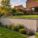 Mur de soutènement enduit séparant deux niveaux de jardin derrière une maison en brique, avec chaperon en pierre bleue et barbacanes en pied